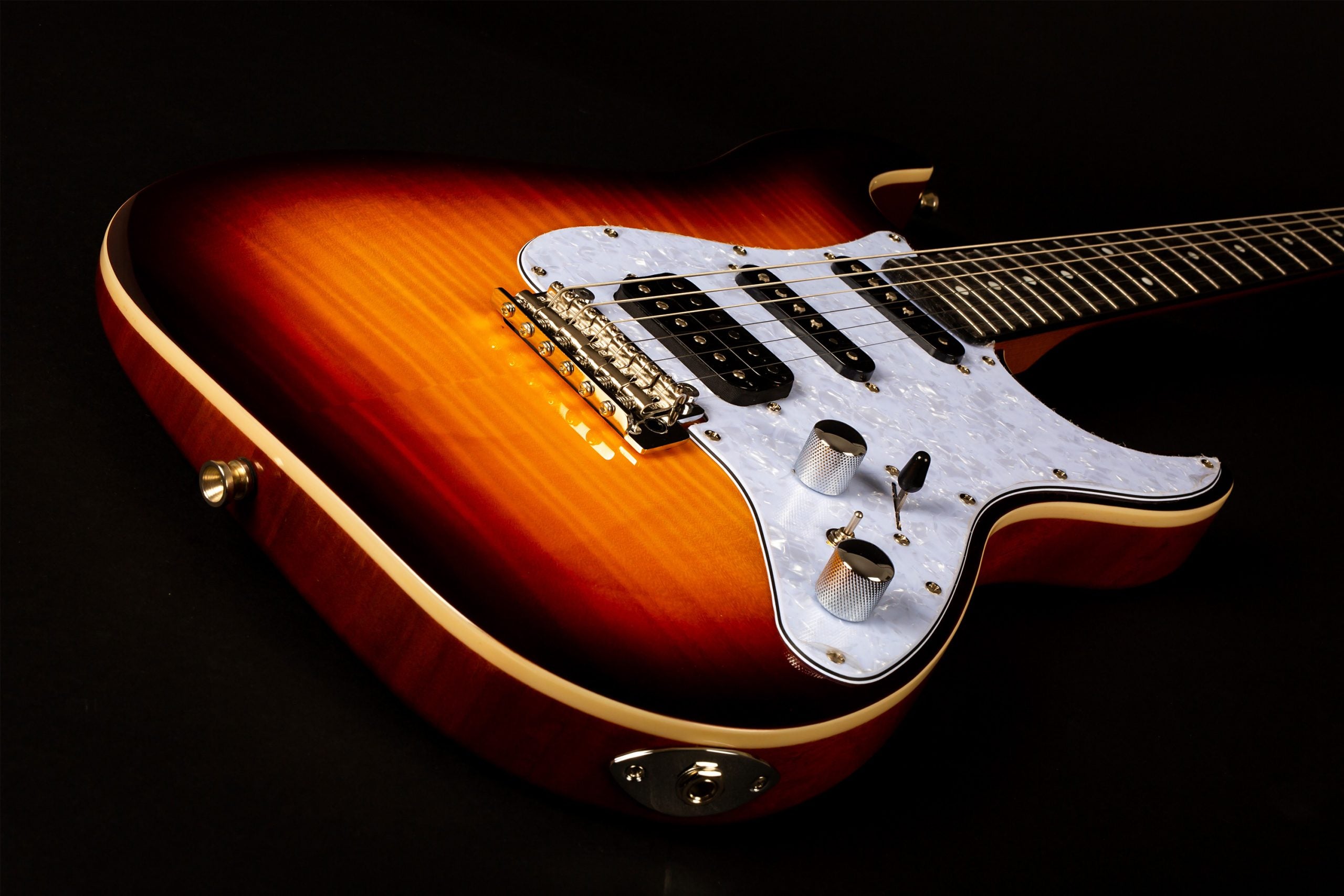 Sunburst electric guitar with a glossy finish, white pearloid pickguard, chrome knobs, and black pickups, lying on a black background.