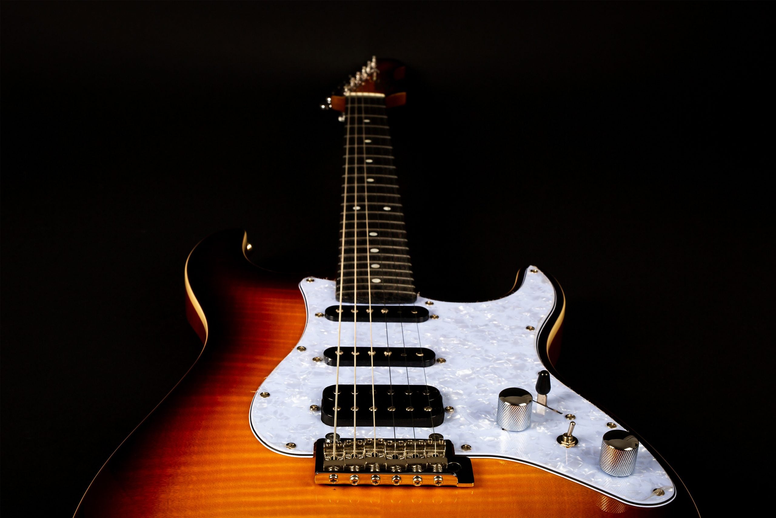 Electric guitar with a glossy sunburst body, white marbled pickguard, three pickups, and silver control knobs against a black background.