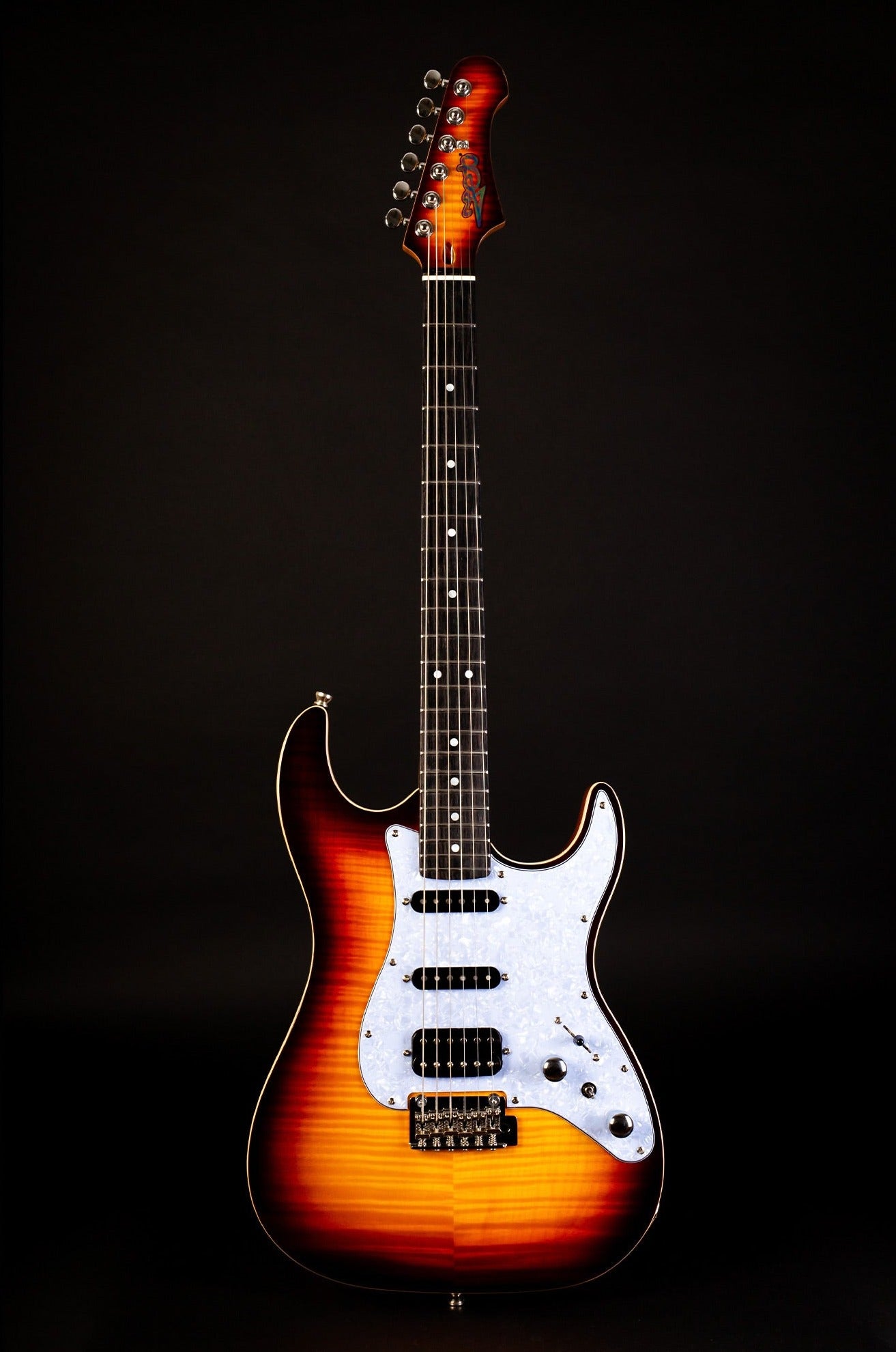 Sunburst electric guitar with a flamed maple finish, three pickups, white pearloid pickguard, and chrome hardware against a black background.