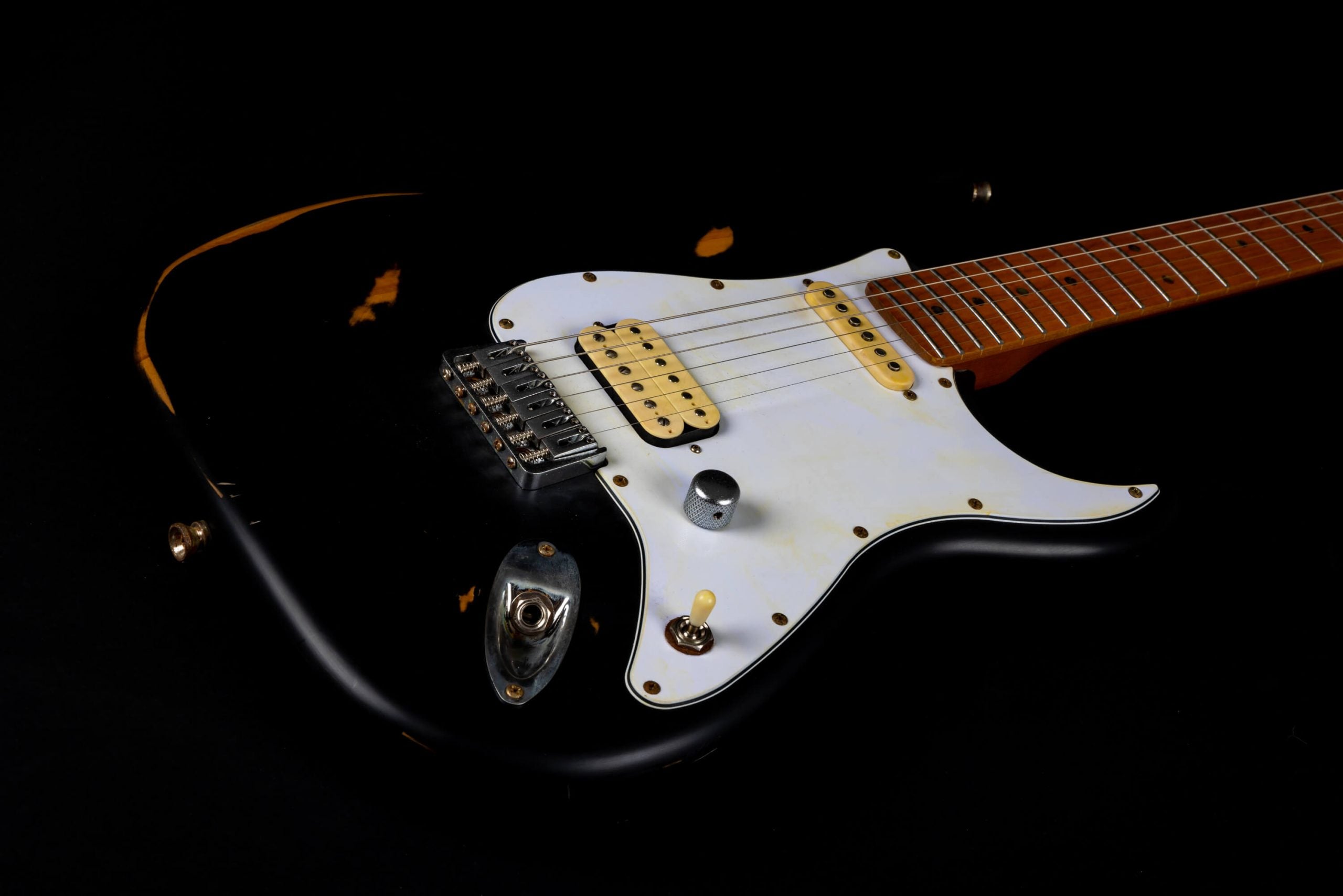 Black electric guitar with a white pickguard, single volume knob, three pickups, and visible wear marks exposing wood underneath.