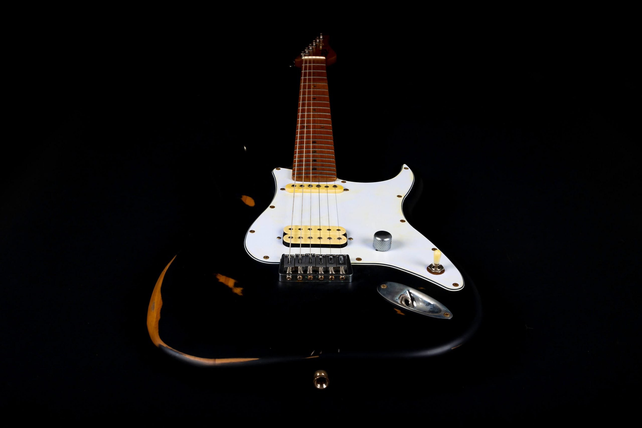 Black electric guitar with a white pickguard, maple neck, six strings, and some wood wear showing on the body edges.