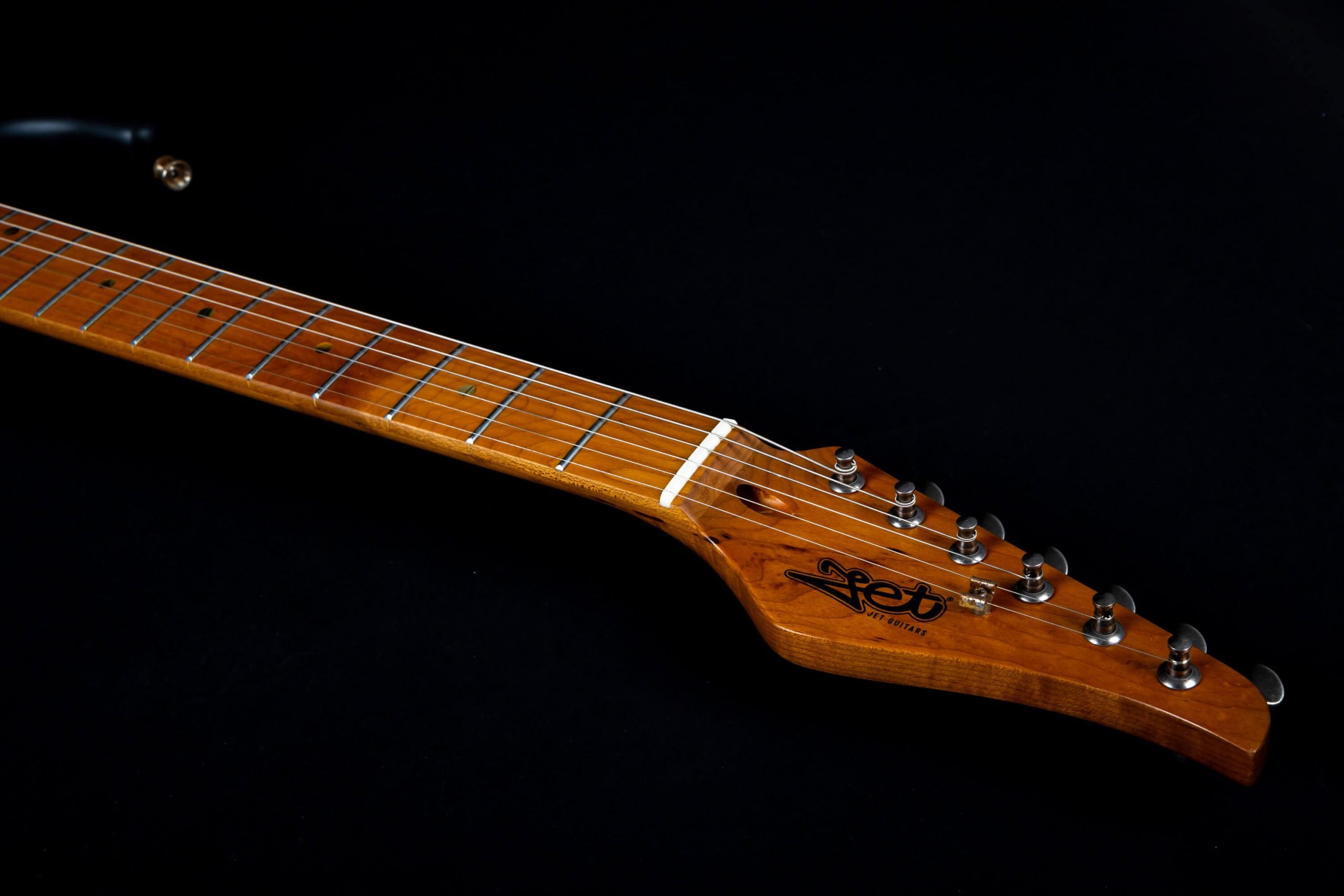 Light brown electric guitar neck and headstock with six metal tuning pegs and "Jet Guitars" logo, set against a black background.