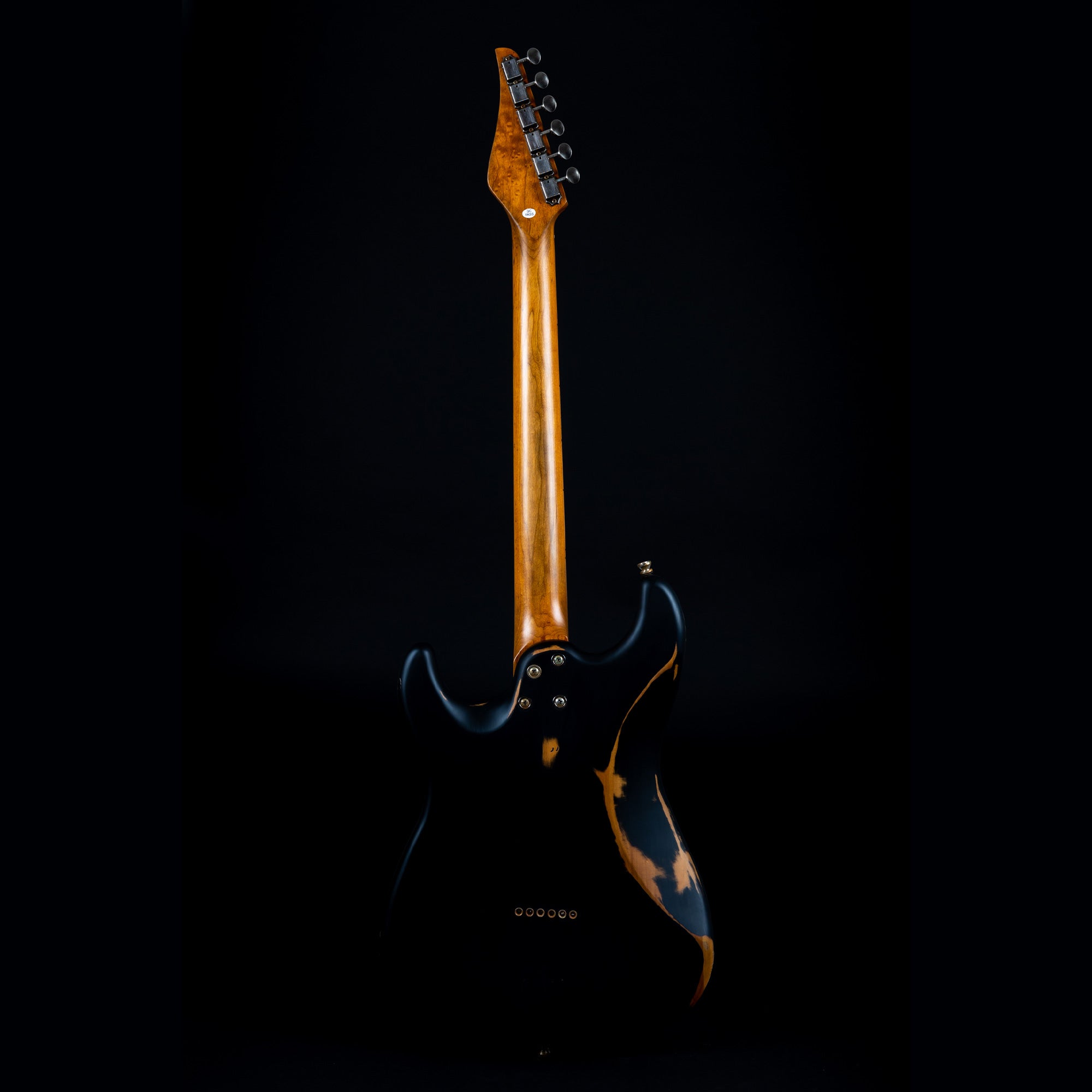 Electric guitar with a natural wood neck and a black body featuring worn patches that reveal the wood underneath, viewed from the back.