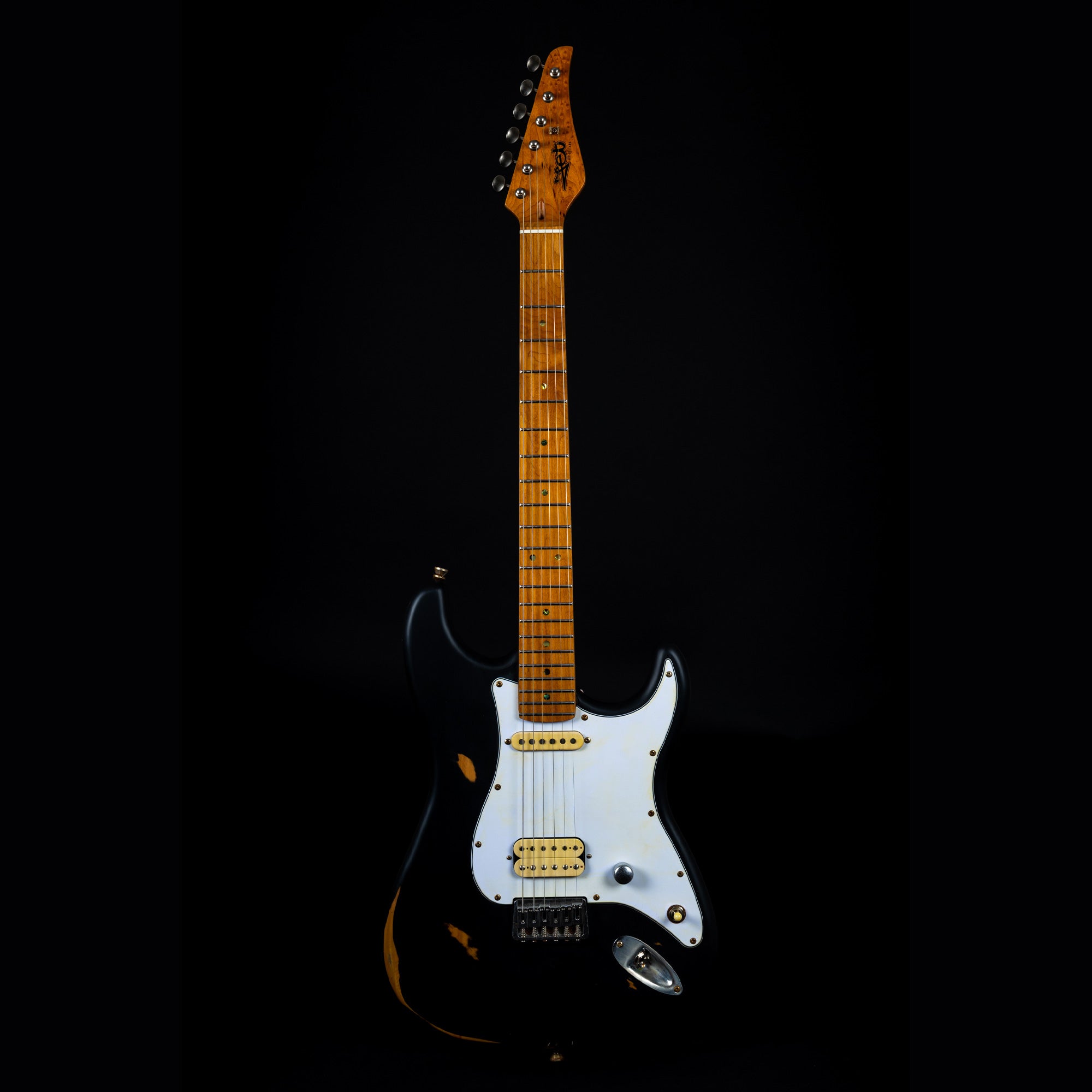 Black electric guitar with a white pickguard, six strings, and a maple neck featuring visible wear and vintage-style hardware.