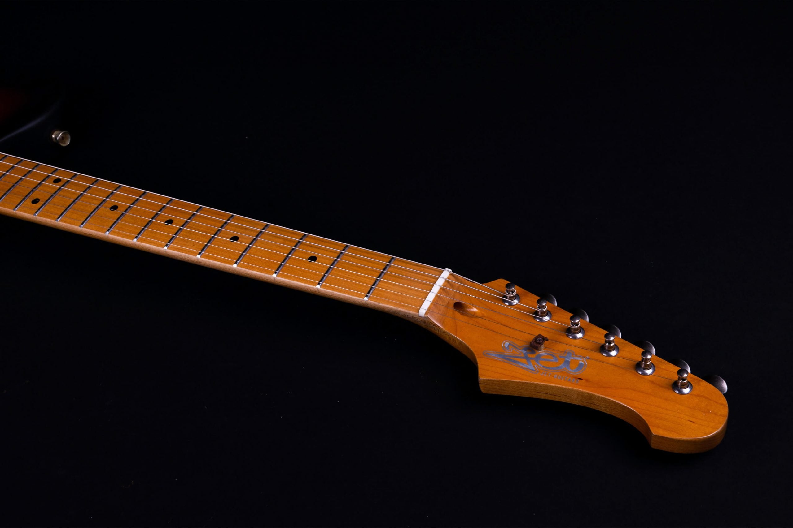 Light brown electric guitar neck with six metal tuning pegs, silver frets, and dot inlays on a black background.