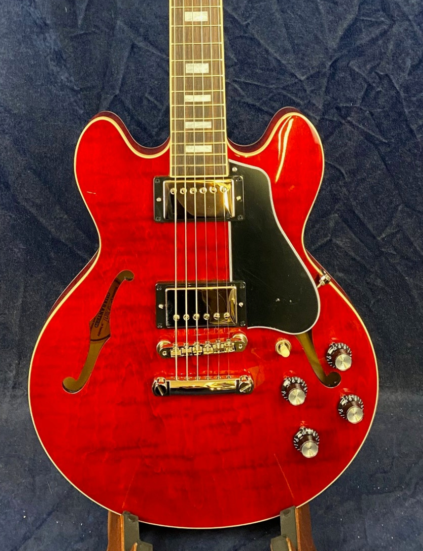 Cherry red semi-hollow electric guitar with black pickguard, two humbucker pickups, four control knobs, and classic f-shaped sound holes.