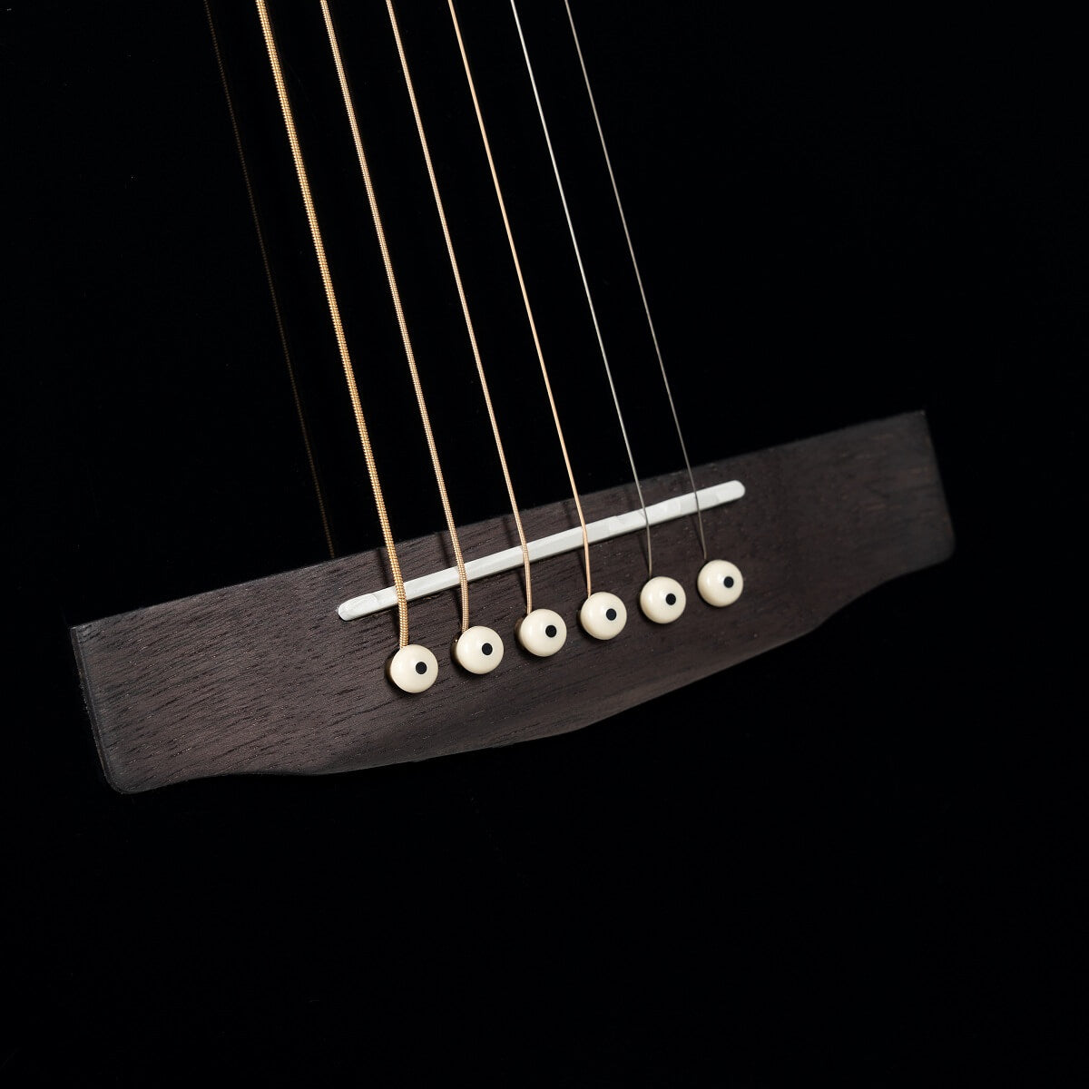 Gros plan sur le chevalet d’une guitare acoustique noire avec six cordes fixées par des chevilles blanches.