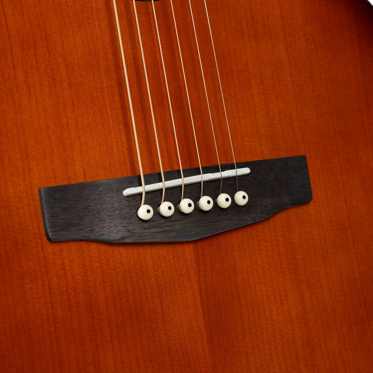 Close-up of an acoustic guitar bridge, showing six strings anchored by white bridge pins on a dark wooden base against a warm brown body.