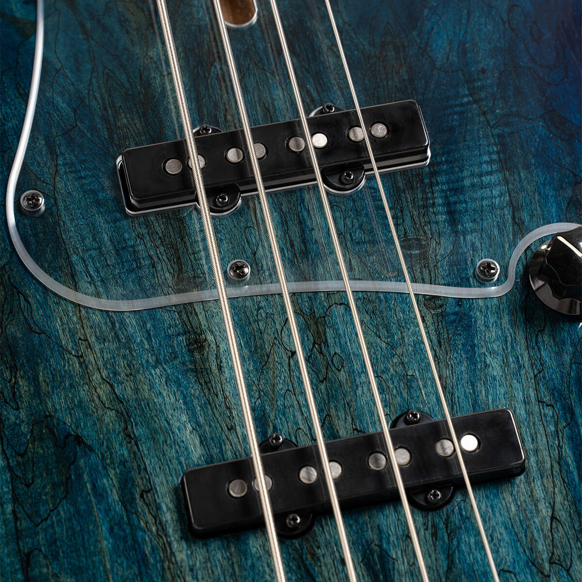 Four metal strings, black pickups with silver dots, and a control knob sit on blue-green wood grain; this is an electric bass close-up.