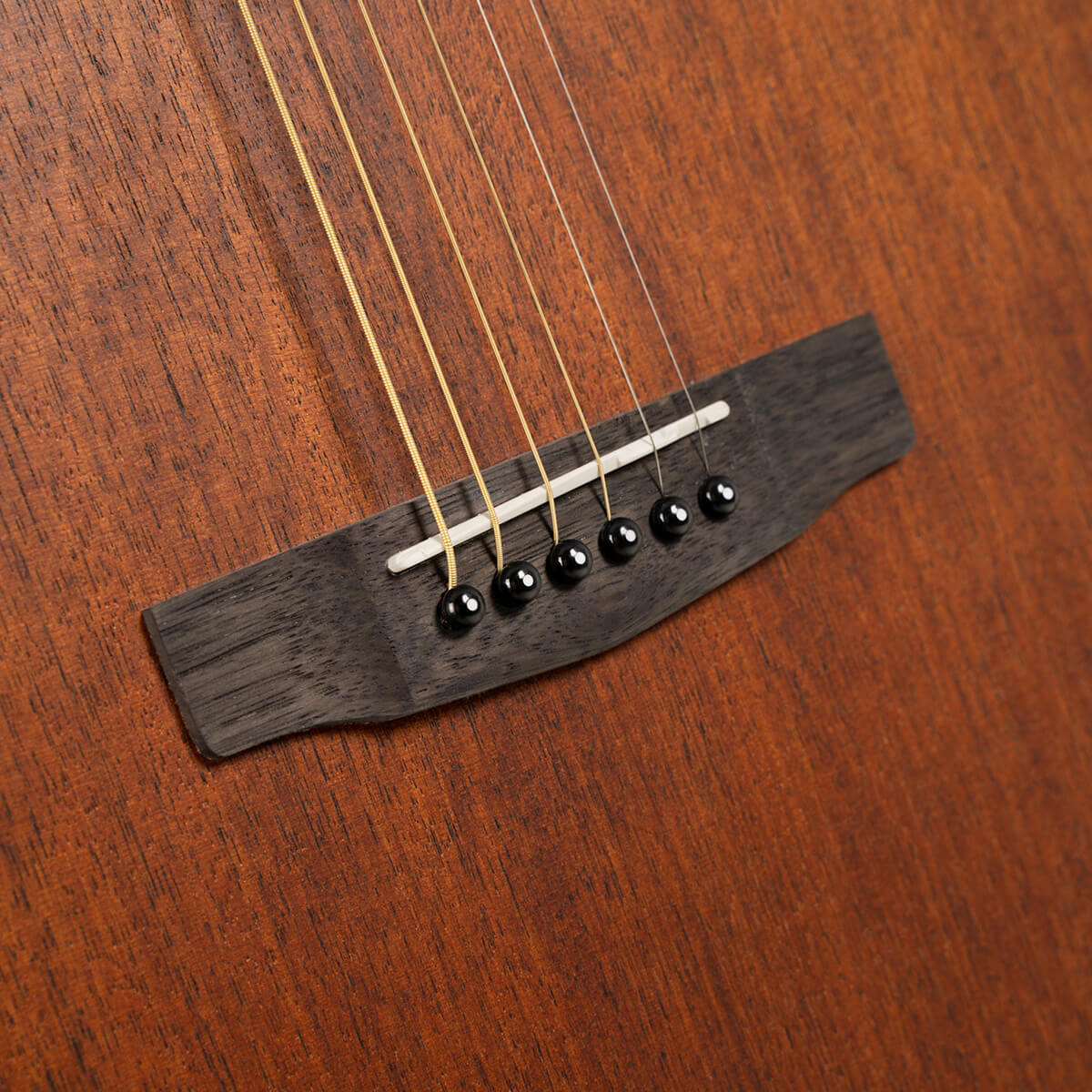 Close-up of an acoustic guitar bridge with six strings, black bridge pins, and a wooden body in a natural brown finish.