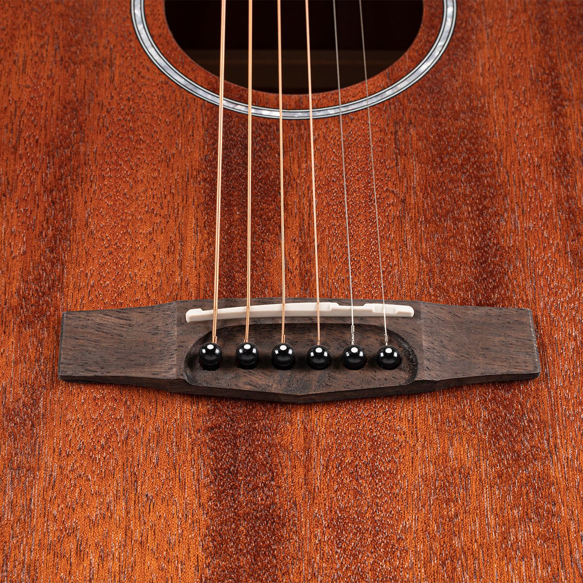 Close-up of an acoustic guitar bridge with six strings, black bridge pins, and a white saddle on a rich, reddish-brown wooden body.