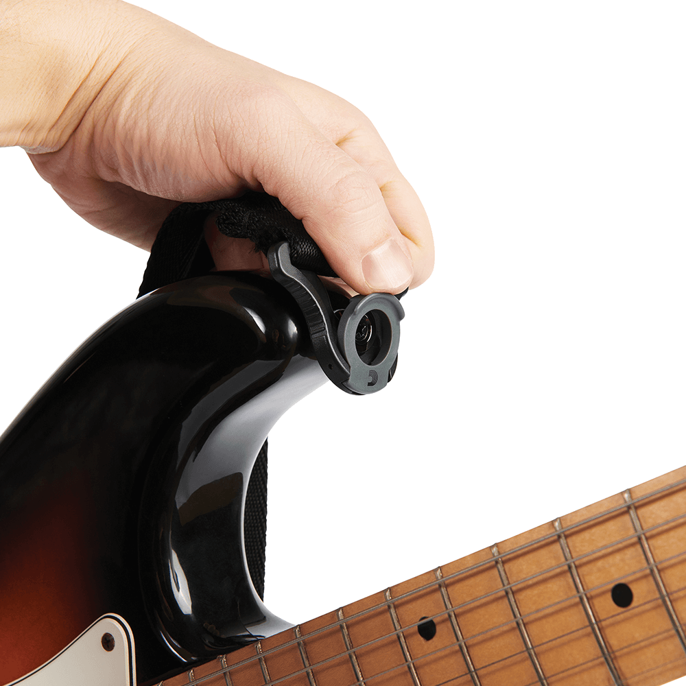 A hand attaches a strap lock accessory to the strap button on the upper body of an electric guitar, securing the instrument strap in place.