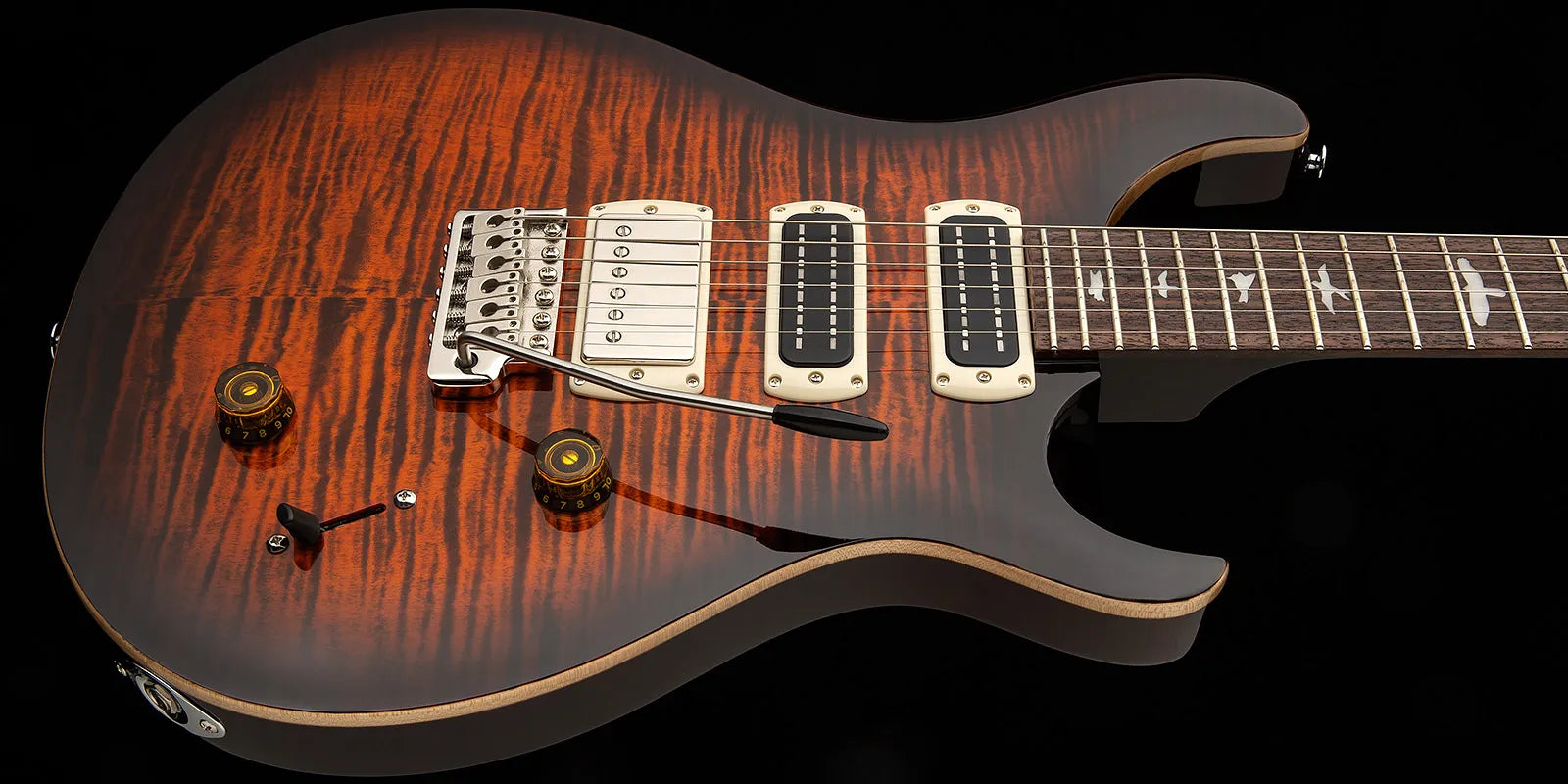 Electric guitar with a glossy, flame maple orange-brown top, three pickups, tremolo arm, two knobs, and fretboard inlaid with bird shapes.
