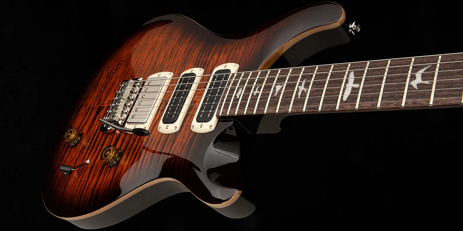 Electric guitar with a glossy brown wood finish, three pickups, bird inlays on the fretboard, and two amber control knobs.