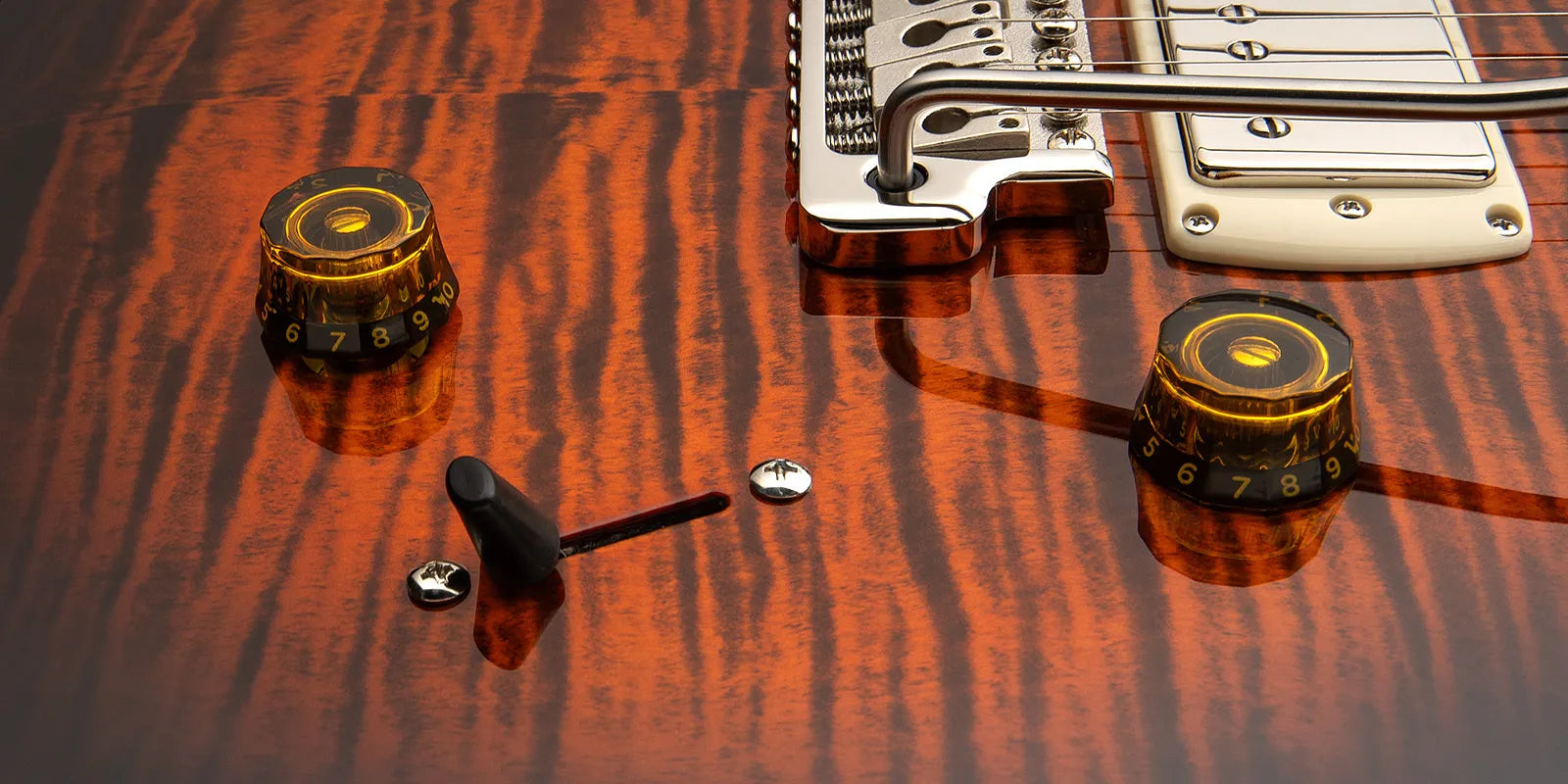 Glossy electric guitar body with a striped amber wood finish, two amber control knobs numbered 0-10, a black switch, and chrome hardware.