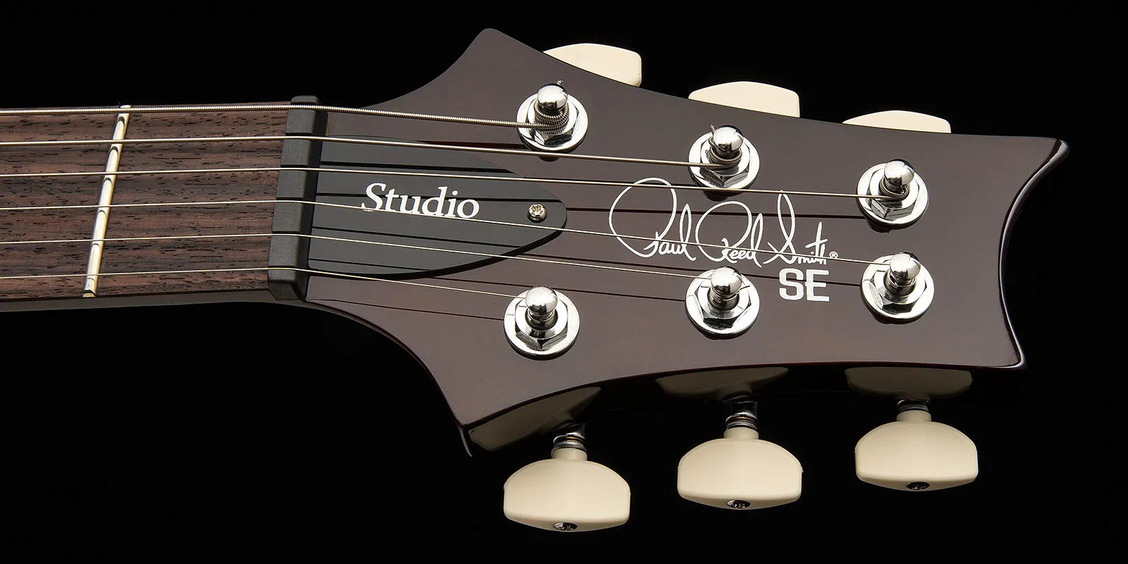 Close-up of Paul Reed Smith SE electric guitar headstock, dark wood finish, six tuning pegs, “Studio” label, and signature logo on the front.