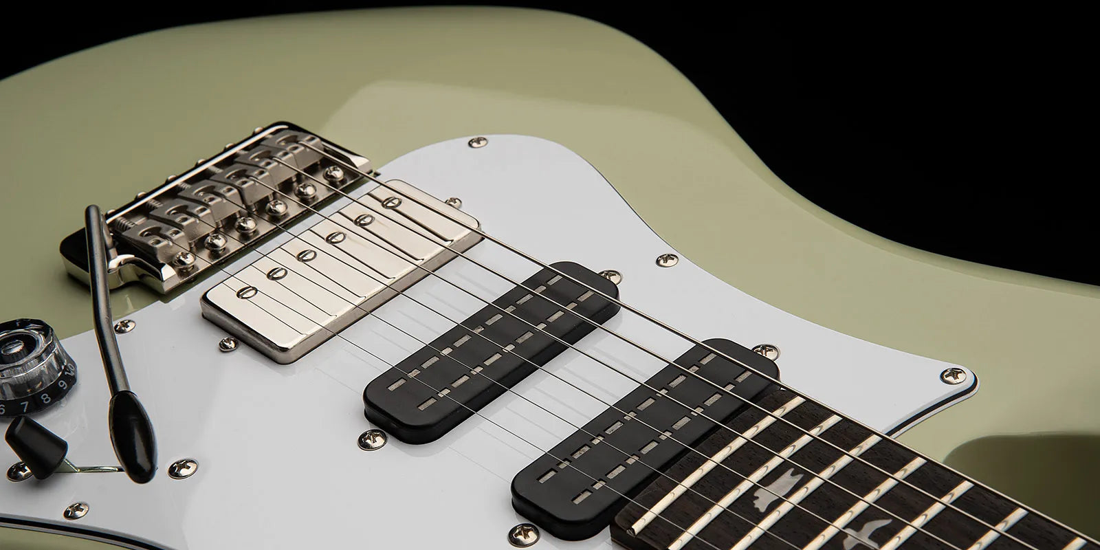 Close-up of a Paul Reed Smith electric guitar showing bridge, three pickups, whammy bar, control knob, and pale green body with white pickguard.