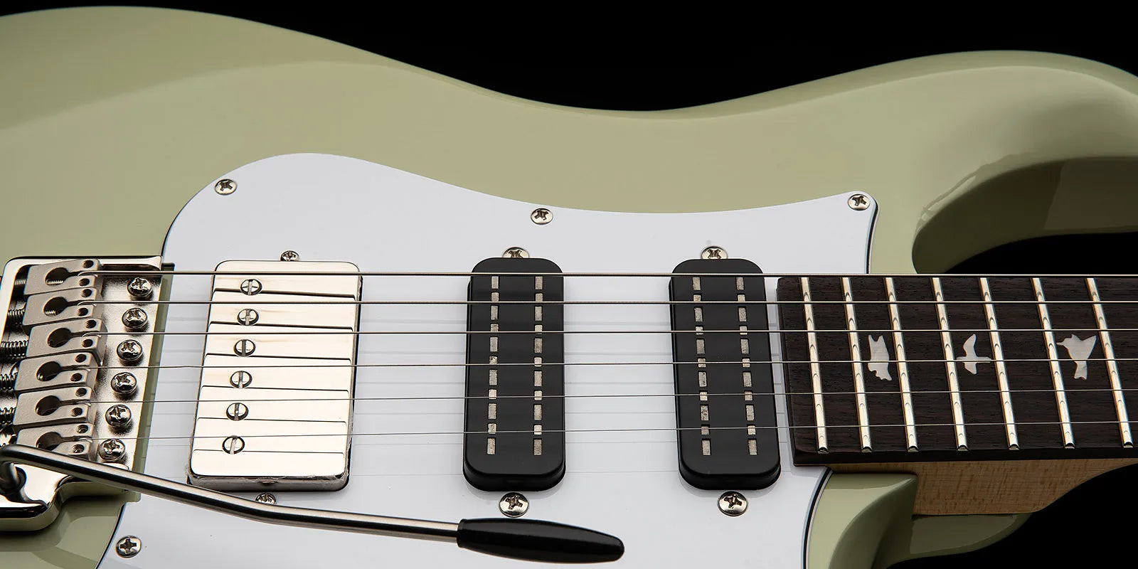 Closeup of a Paul Reed Smith electric guitar showing strings, three pickups, white pickguard, and fretboard with bird-shaped inlays.