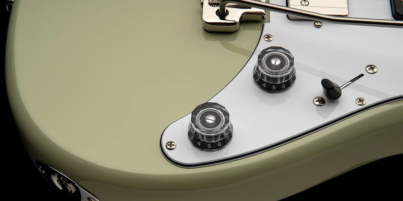 Close-up of a Paul Reed Smith electric guitar showing two numbered control knobs, a toggle switch, and part of a white pickguard on a pale body.