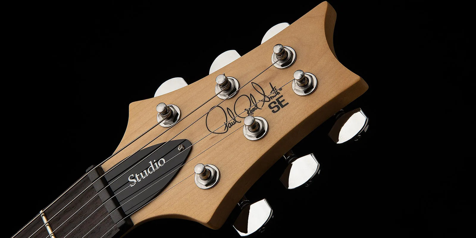 Close-up of a Paul Reed Smith SE electric guitar headstock, six tuning pegs, signature logo, and “Studio” truss rod cover visible.