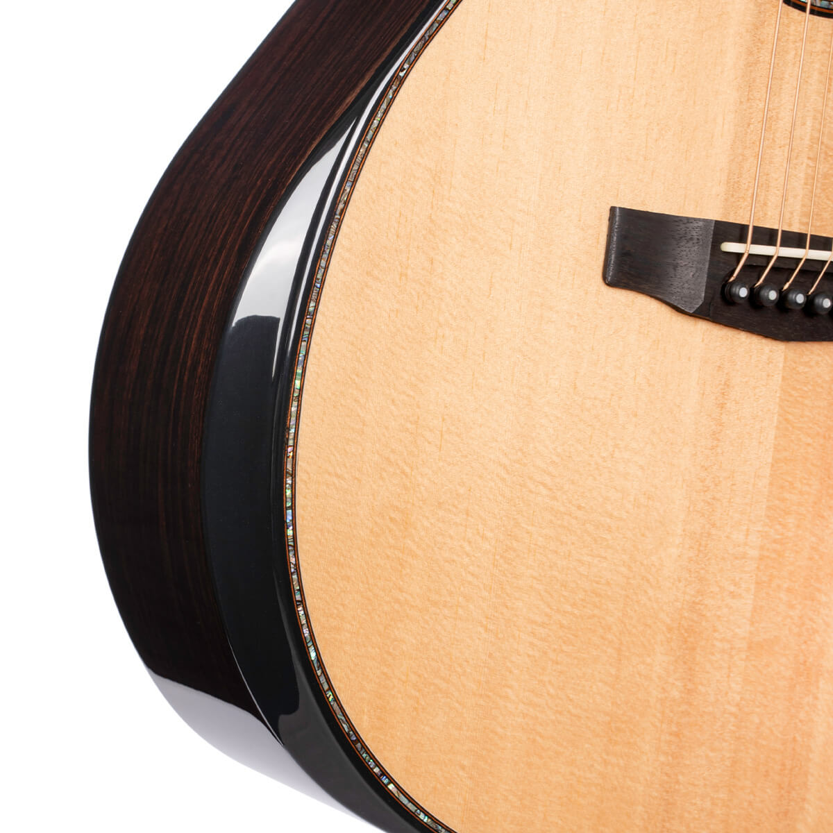 Glossy acoustic guitar body showing a light wood top, dark wood sides, abalone binding, and part of the black bridge with strings attached.