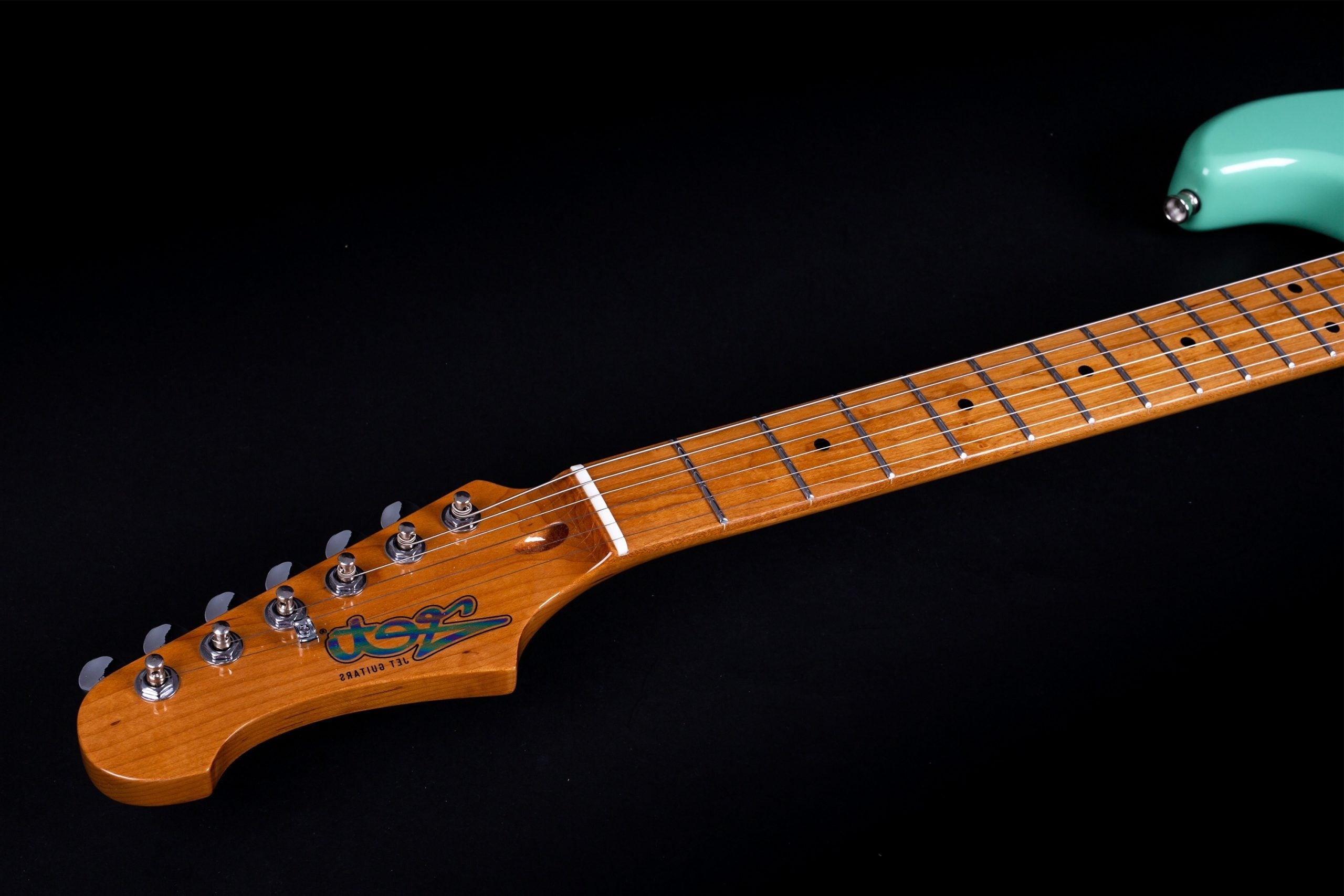 Light brown electric guitar neck and headstock with six silver tuning pegs, dot inlays, and part of a mint green guitar body on the right.