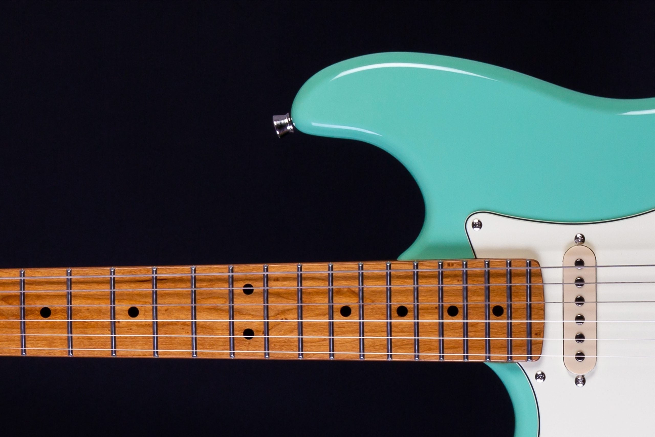 Aqua green electric guitar, partial view showing wooden fretboard with metal frets and white pickguard against a black background.