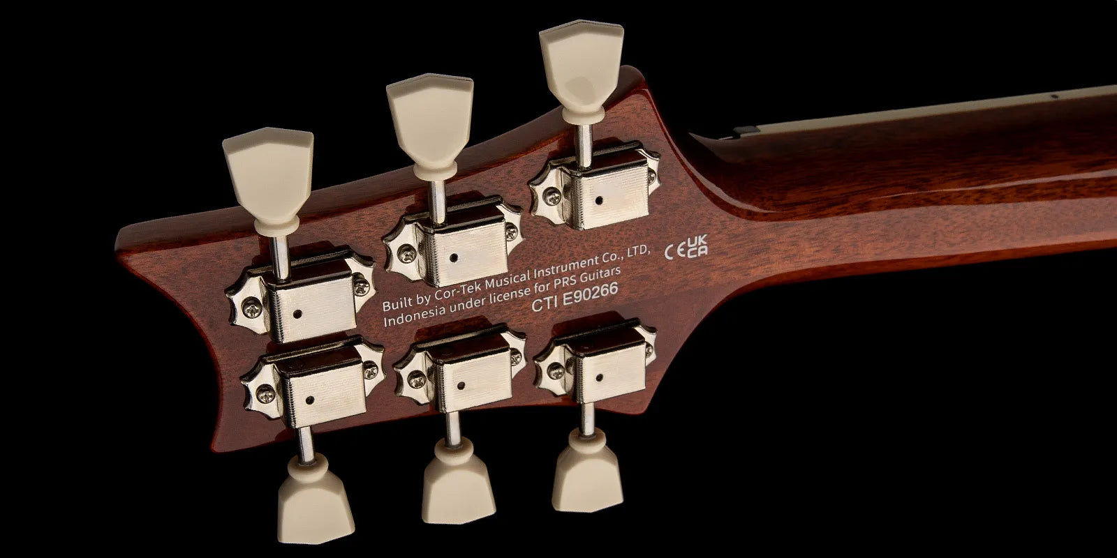 Six vintage-style tuning pegs with cream knobs on a dark wood electric guitar headstock, serial number and manufacturer info printed in white text.