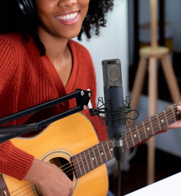 Woman in headphones playing acoustic guitar and singing into a mounted pro audio microphone on a stand.