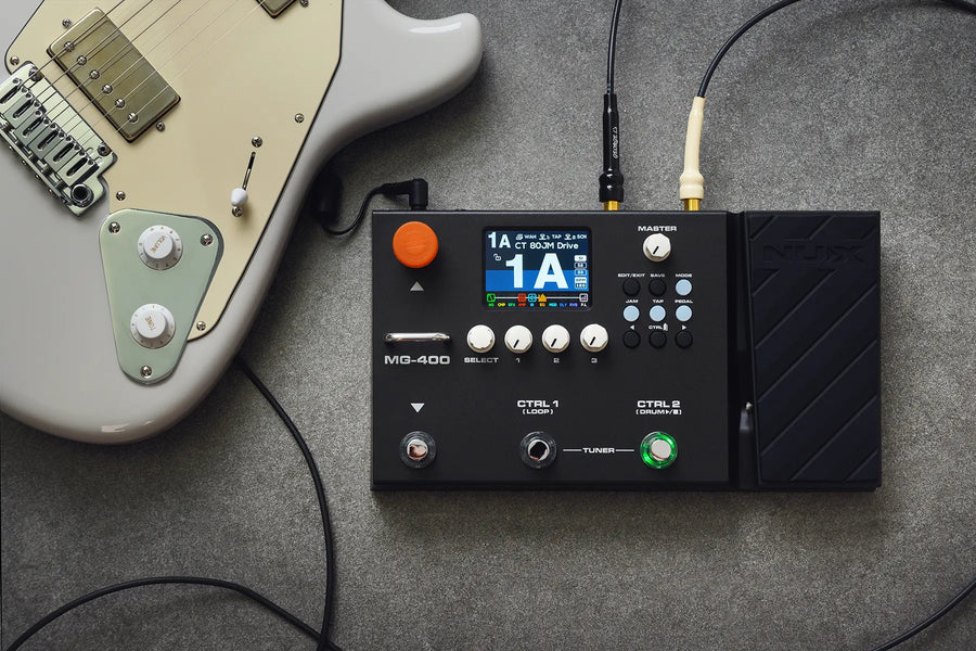 A white electric guitar is next to a NUX MG-400 FX pedal, which features a display screen, knobs, and connected cables on a gray surface.