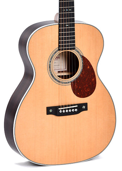 Guitare acoustique à six cordes, caisse claire en bois clair, touches noires et pickguard marron près de la rosace décorative.