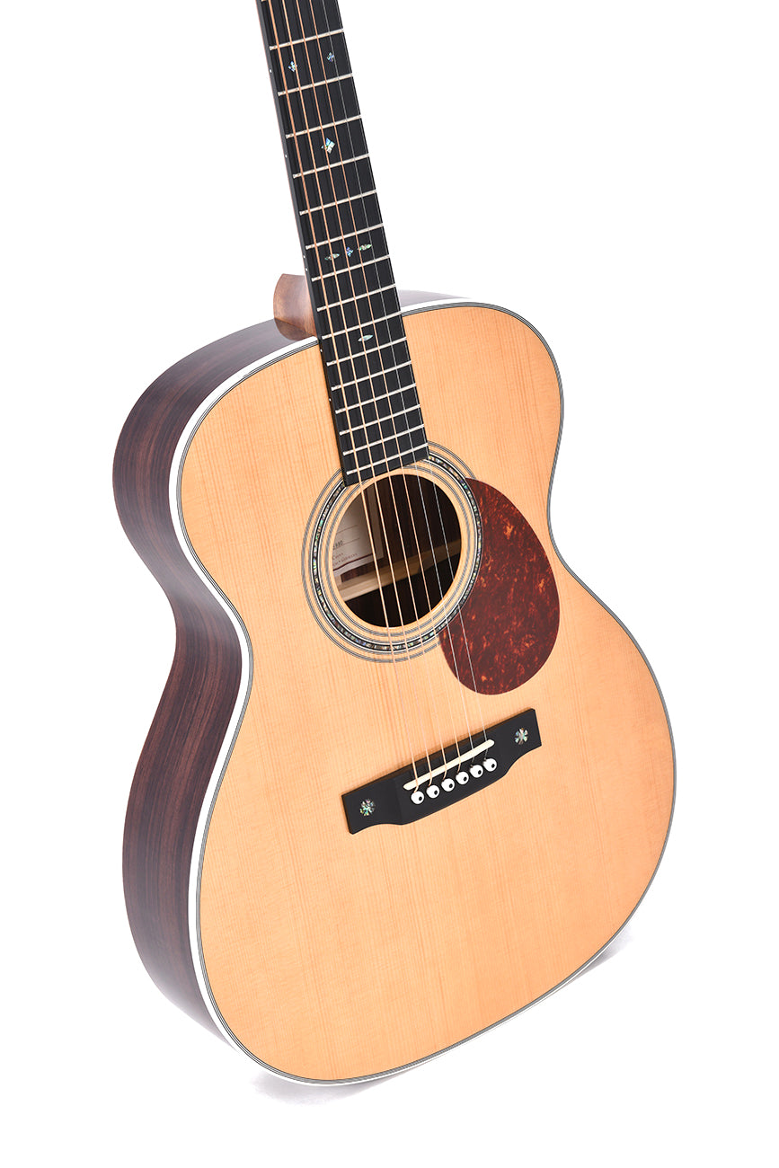 Guitare acoustique à caisse claire en bois clair, dos et éclisses foncés, six cordes, pickguard marron, rosace décorée autour de la bouche.
