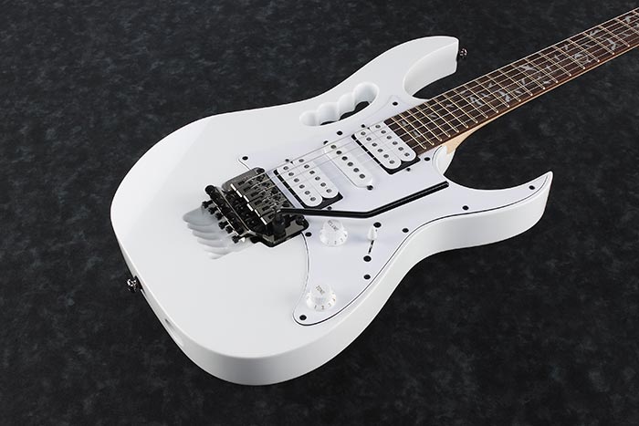 White electric guitar with a whammy bar, three pickups, a handle carved into the body, and white control knobs.