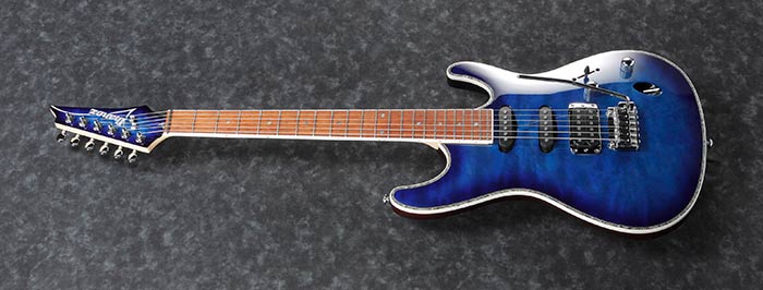 Blue electric guitar with a glossy finish, three pickups, whammy bar, maple fretboard, and chrome hardware against a dark textured background.