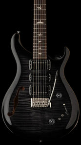 Black electric guitar with three pickups, a whammy bar, bird inlays on the fretboard, and an f-hole on the upper left side of the body.