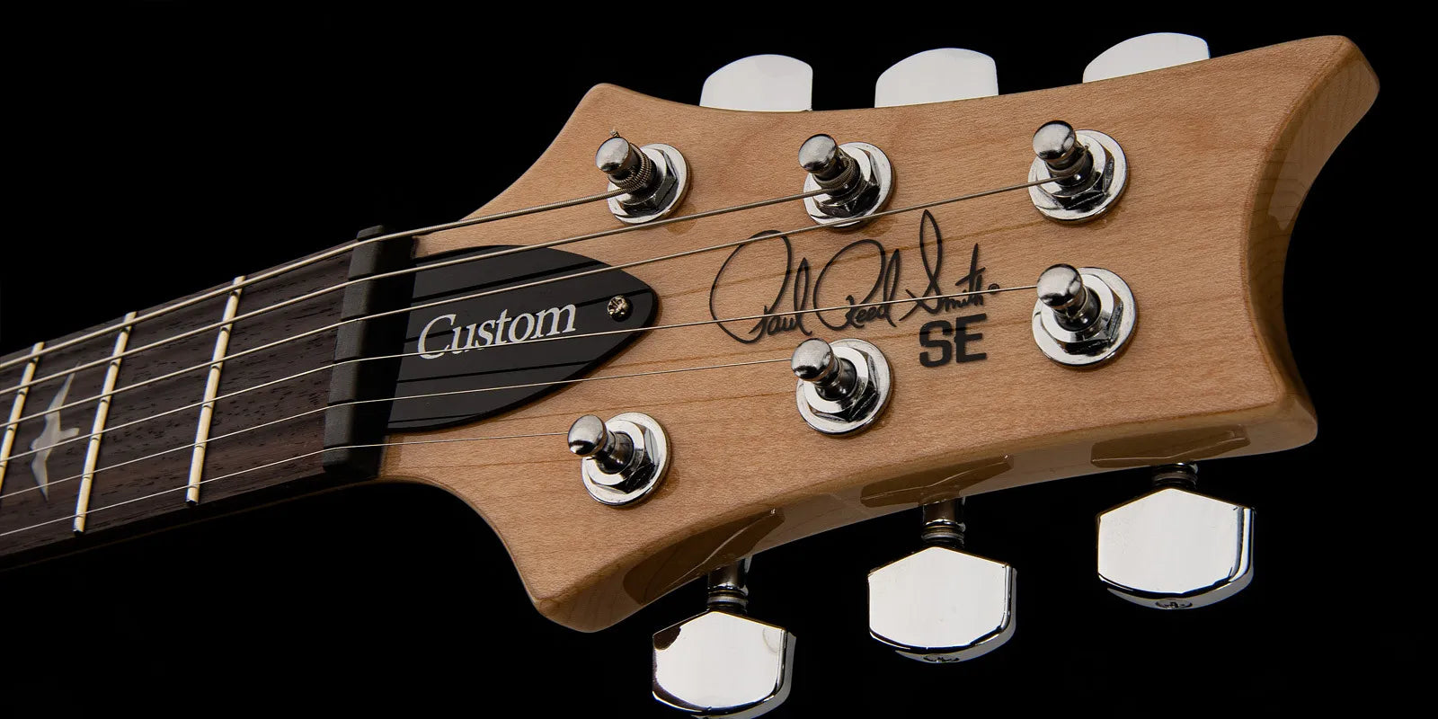 Light wood electric guitar headstock with chrome tuning pegs, "Custom" truss rod cover, and SE series logo with a signature on the front.