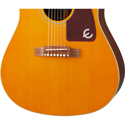 Light brown acoustic guitar body with a dark red pickguard, white decorative letter "E," and white bridge pins on a wooden bridge.