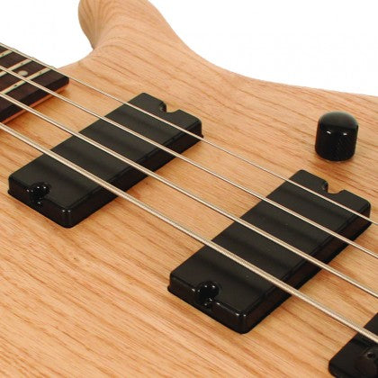 Close-up of a natural wood bass guitar body showing four strings, two black pickups, and one black control knob.