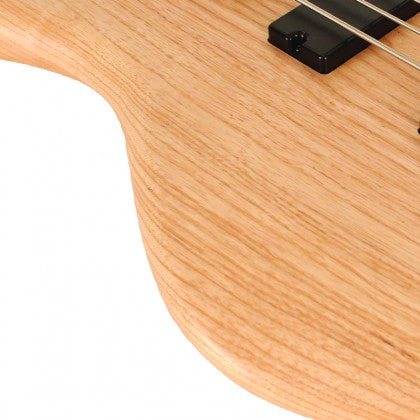 Light wood grain body of a bass guitar with part of a black pickup and metal strings visible in the top right corner.