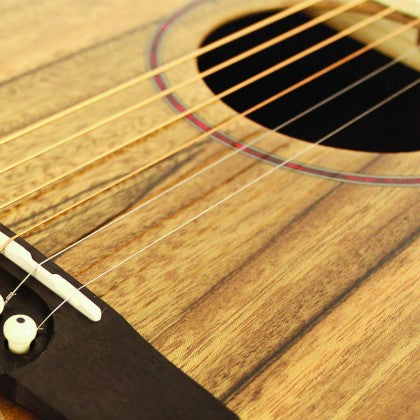Close-up of an acoustic guitar's wooden body, six strings, sound hole with a thin red ring, and part of the black bridge with a white pin.