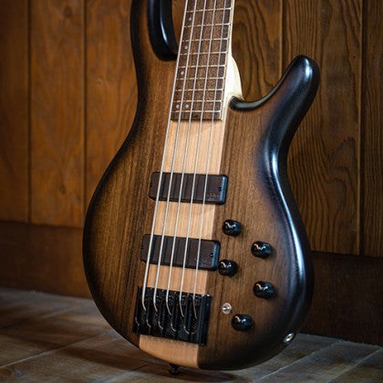 Five-string bass guitar with a dark wood sunburst finish, four control knobs, two pickups, and a natural wood stripe down the center.