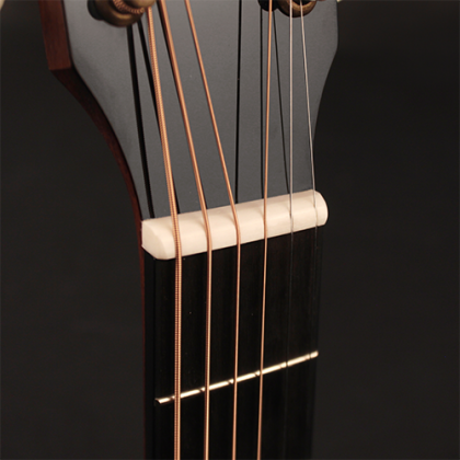 Close-up of an acoustic guitar’s headstock showing six steel strings passing over the nut and the top of a dark wooden fretboard.