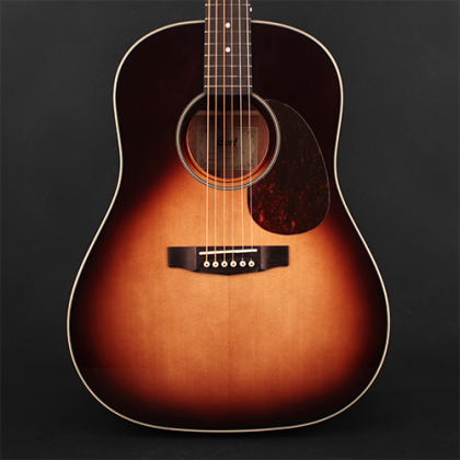 Sunburst-finish acoustic guitar with a rounded body, six strings, white-edged soundhole, dark pickguard, and a wooden bridge with white pins.