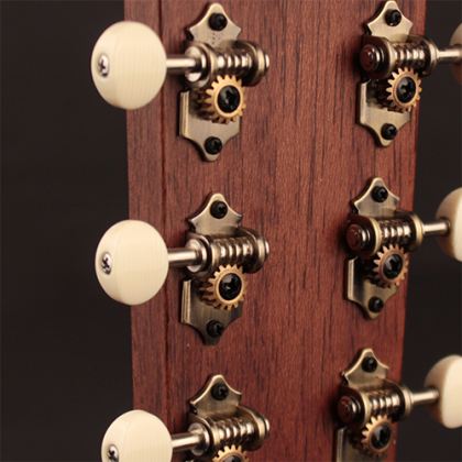 Close-up of an acoustic guitar headstock showing six metal tuning pegs with white knobs and exposed gears against a wooden background.