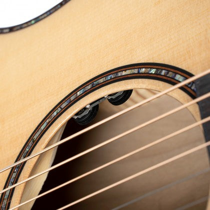 Close-up of an acoustic guitar's soundhole showing detailed inlay, strings, and two control knobs inside the body.