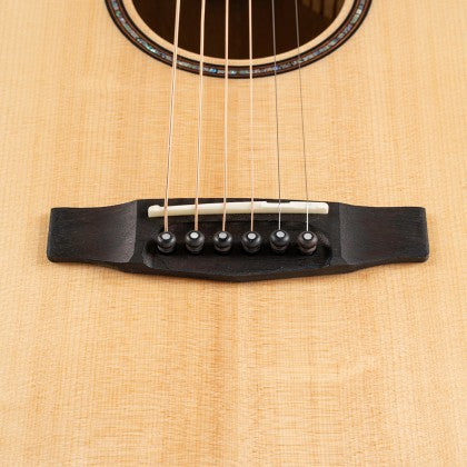 Close-up of an acoustic guitar bridge with six strings, black bridge pins, and a light wood body.