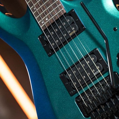 Close-up of a teal electric guitar showing pickups, strings, and whammy bar with a sparkly finish.