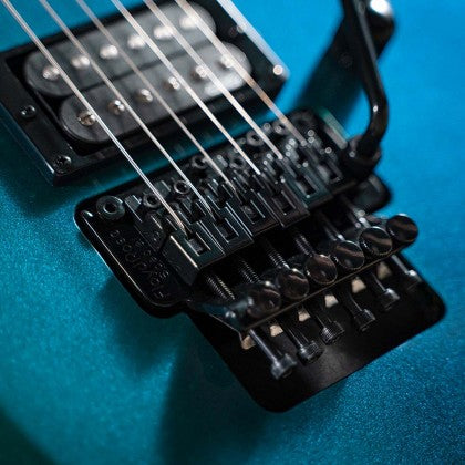 Close-up of an electric guitar’s bridge and tremolo system on a metallic blue body, showing strings, fine tuners, and pickup screws.