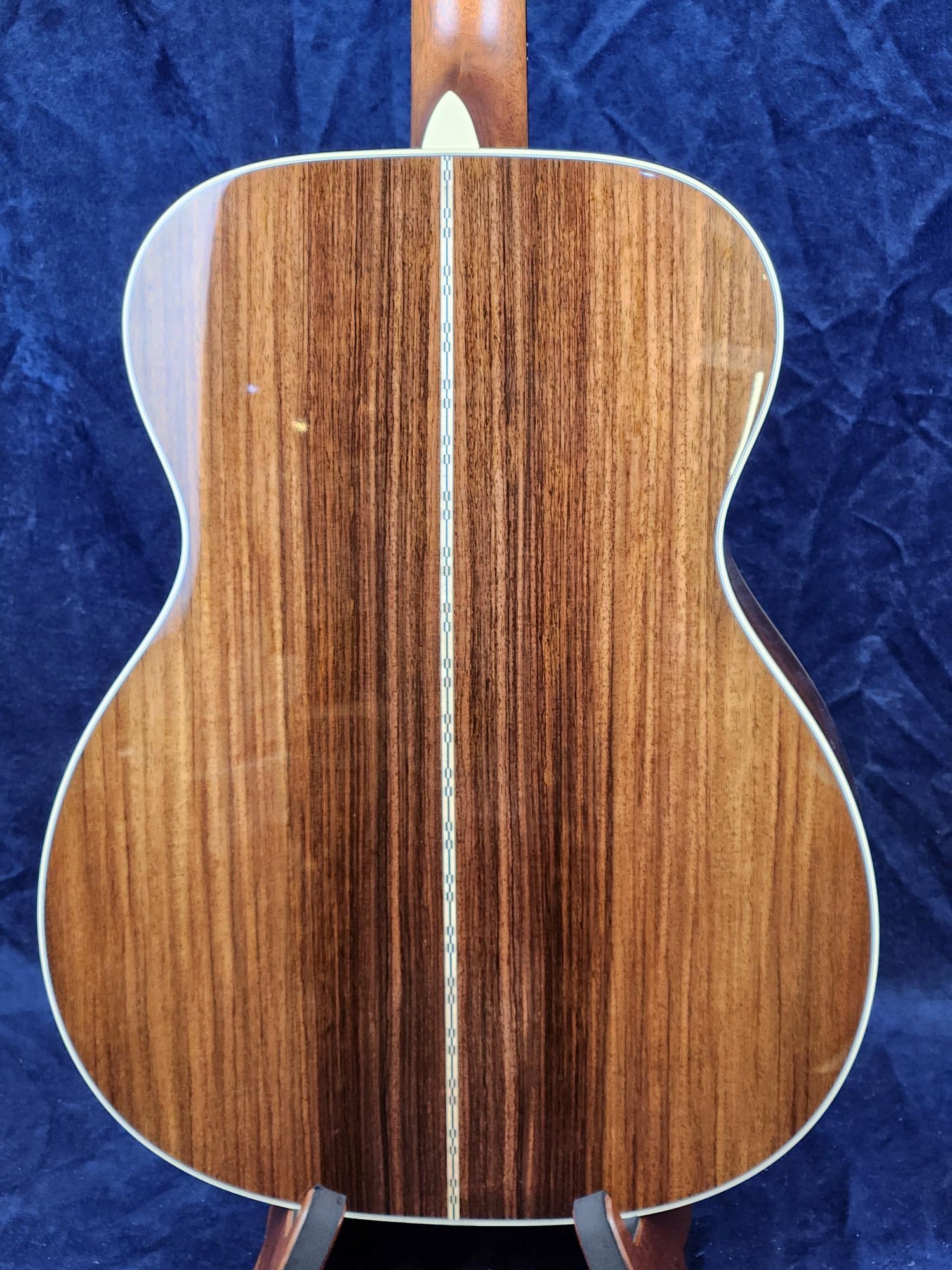Back of an acoustic guitar with glossy, dark wood finish, light binding around the edges, and a decorative inlay strip running down the center.