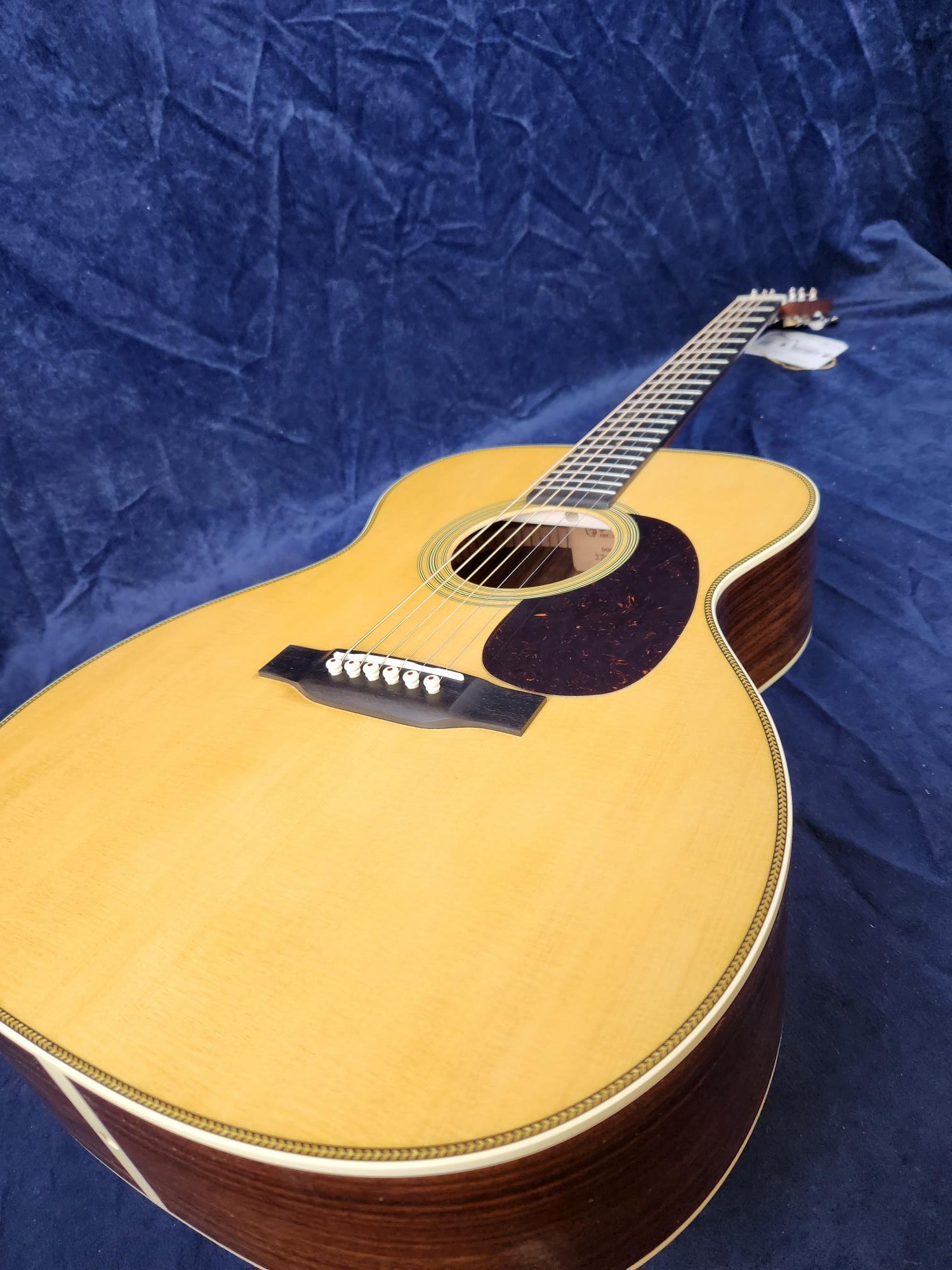 Acoustic guitar with a light wood top, dark wood sides, white binding, and a dark pickguard, resting on a textured blue background.